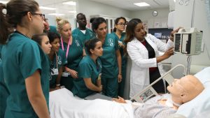 students during a nursing class practical session listening to their teacher demonstrating on patient monitoring equipment use